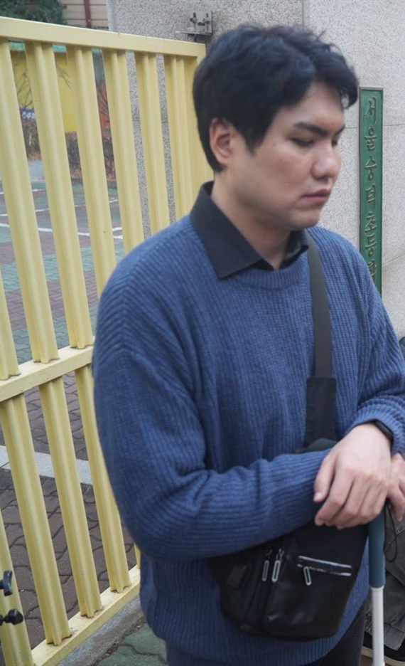 배우 이창훈이 단편영화 〈새로고침〉 촬영 현장, 초등학교 정문 앞에서 흰지팡이를 짚고 서 있는 모습.